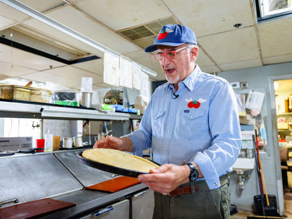 Ralph holds a pan with a pizza crust in it.