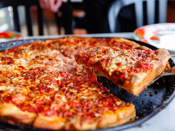 A piece of pizza being lifted from a pan.