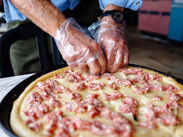 Ralph puts toppings on a sausage pizza.