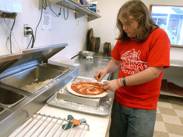 A Gumby's employee puts pepperoni on a pizza.