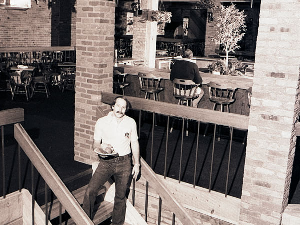 The owner of Josie's Pizza Kitchen stands on a staircase inside the restaurant.