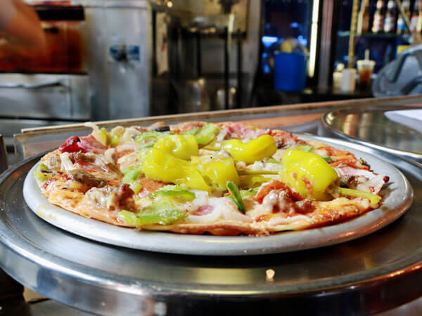 A pizza on a pan topped with meat and veggies.