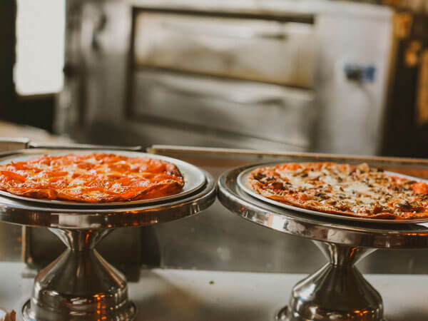 Two pizzas sit on stands on a bar.