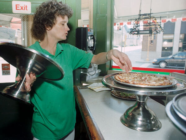 A waitress places a pizza on a stand.