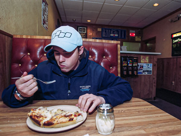 A student eats pizza in a booth.