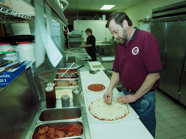 The owners of Micheleo's prep pizzas with toppings.