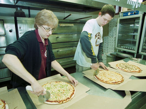 Two Micheleo's employees slice pizzas.