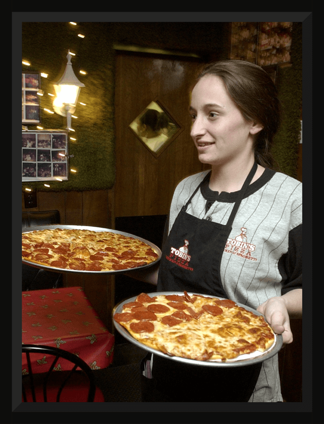 A young waitress carries two Tobin's pizzas.