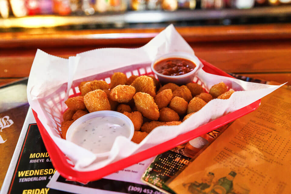 Basket of fried appetizers with two dipping sauces on a bar counter.