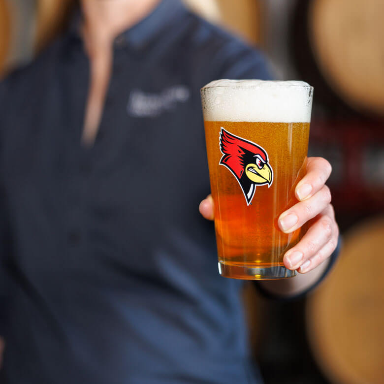 Person holding a pint glass of beer with a Reggie Redbird logo.