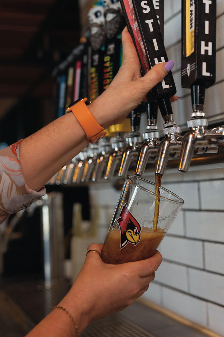 A person pouring beer from a tap into a glass with a Reggie Redbird logo.