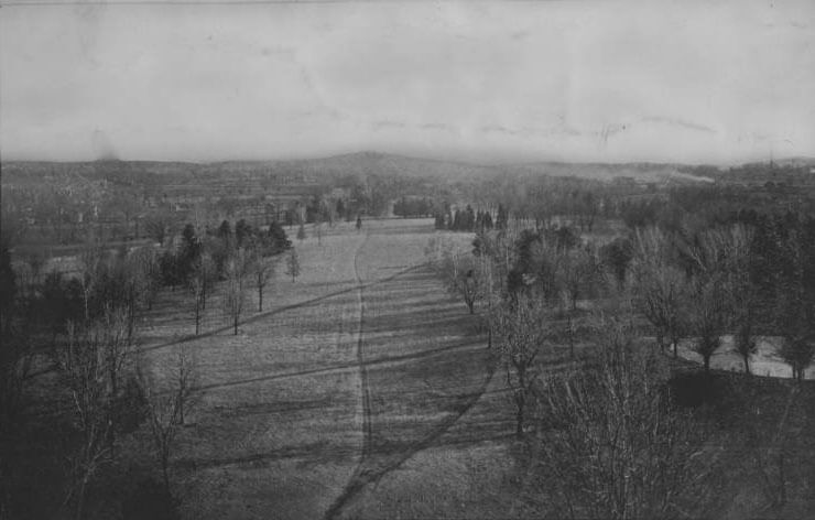 Black and white photo of a rural landscape with a field, trees, and distant hills.