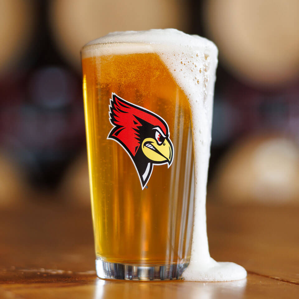 A person pours beer into a pint glass with a Reggie Redbird logo.