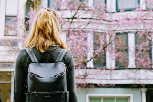 a woman wearing a backpack seen from behind - with rose blossoms in the background