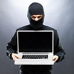 a man in a black mask holds a laptop menacingly