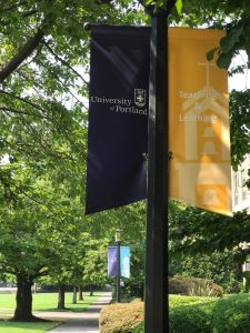 Photo of the University of Portland courtyard path with two flags, UP & Teaching and Learning.